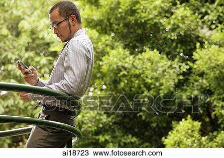 Businessman leaning on railing, using mobile phone, text messaging View Large Photo Image Stock Image - Businessman leaning on railing, using mobile phone, text messaging. Fotosearch