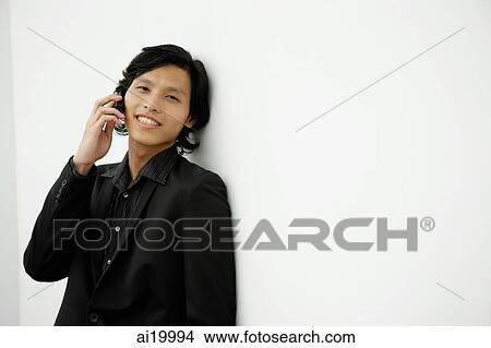 Businessman leaning on wall, using mobile phone, smiling View Large Photo Image Picture - Businessman leaning on wall, using mobile phone, smiling. Fotosearch