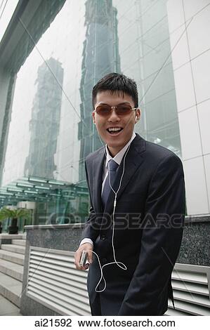 Businessman listening to MP3 player, smiling at camera View Large Photo Image Stock Image - Businessman listening to MP3 player, smiling at camera. Fotosearch