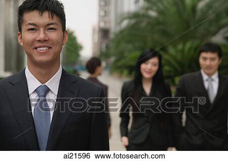 Businessman looking at camera, people in the background View Large Photo Image Stock Photograph - Businessman looking at camera, people in the background. Fotosearch