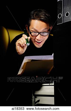Stock Image - Businessman looking at documents at night with flashlight. Fotosearch