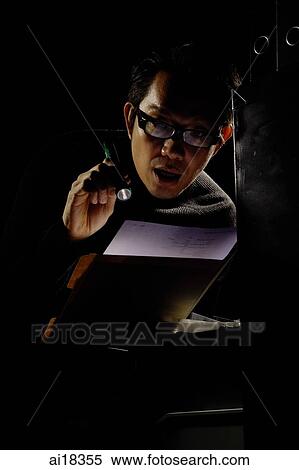 Stock Photography - Businessman looking at documents in the dark with flashlight. Fotosearch