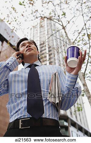Stock Image - Businessman on the phone, holding cup of coffee and newspaper. Fotosearch