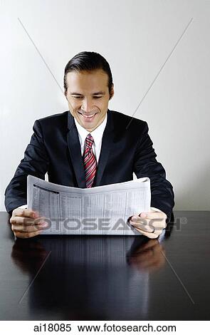 Businessman sitting at table reading newspaper, smiling View Large Photo Image Stock Photography - Businessman sitting at table reading newspaper, smiling. Fotosearch