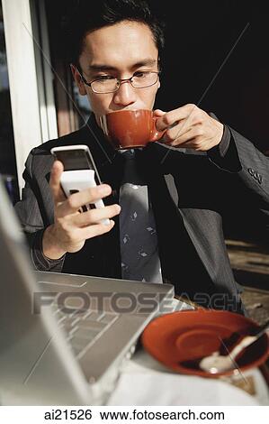 Businessman sitting in front of laptop, using mobile phone and drinking from cup View Large Photo Image Stock Photograph - Businessman sitting in front of laptop, using mobile phone and drinking from cup. Fotosearch