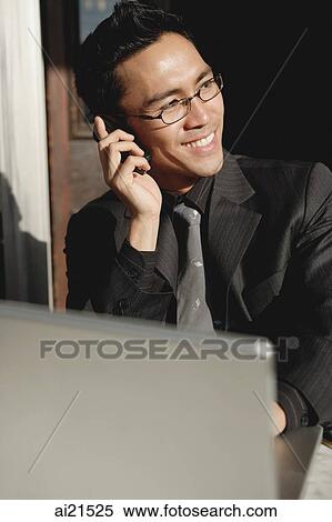 Businessman sitting in front of laptop, using mobile phone, smiling View Large Photo Image Stock Photography - Businessman sitting in front of laptop, using mobile phone, smiling. Fotosearch