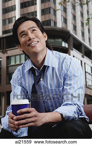 Businessman sitting in the city, holding disposable coffee cup View Large Photo Image Stock Photo - Businessman sitting in the city, holding disposable coffee cup. Fotosearch