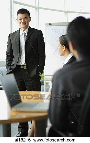Businessman standing before seated colleagues, smiling at camera View Large Photo Image Stock Photograph - Businessman standing before seated colleagues, smiling at camera. Fotosearch