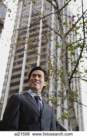 Businessman standing in the city, tree and building behind him View Large Photo Image Stock Photograph - Businessman standing in the city, tree and building behind him. Fotosearch