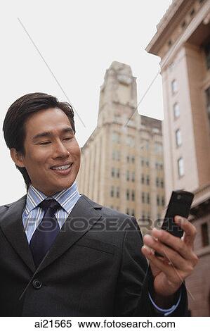 Businessman standing in the city using mobile phone, text messaging View Large Photo Image Stock Photography - Businessman standing in the city using mobile phone, text messaging. Fotosearch