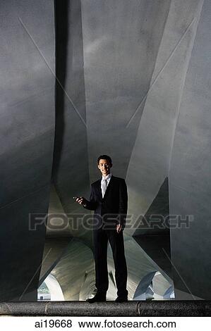 Businessman standing in tunnel, holding mobile phone, smiling at camera View Large Photo Image Stock Photo - Businessman standing in tunnel, holding mobile phone, smiling at camera. Fotosearch