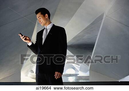 Picture - Businessman standing in tunnel, looking at mobile phone. Fotosearch