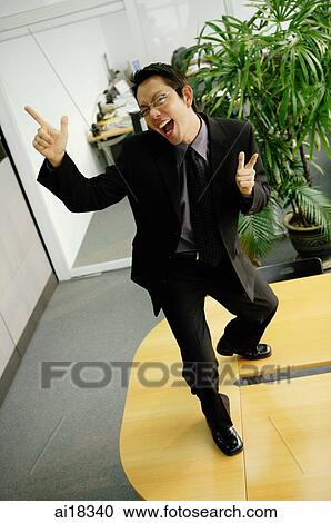 Businessman standing on office desk, making hand signs, mouth open View Large Photo Image Stock Image - Businessman standing on office desk, making hand signs, mouth open. Fotosearch