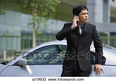 Stock Image - Businessman using mobile phone, leaning on car. Fotosearch