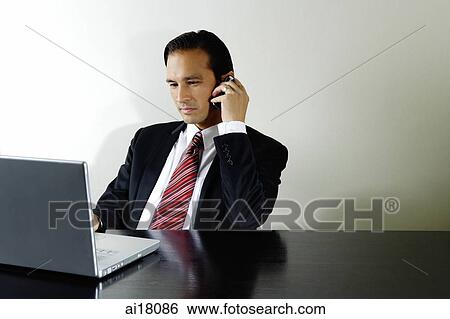 Stock Photograph - Businessman using mobile phone, looking at laptop. Fotosearch