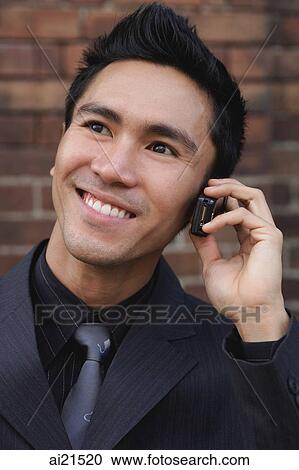 Stock Image - Businessman using mobile phone, smiling, looking away. Fotosearch