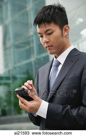 Stock Image - Businessman using PDA, city location. Fotosearch