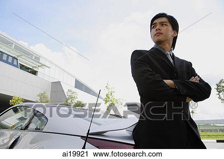 Businessman with arms crossed, leaning on car, looking away View Large Photo Image Stock Image - Businessman with arms crossed, leaning on car, looking away. Fotosearch