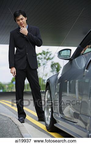 Businessman with hand on chin, looking at car View Large Photo Image Stock Photo - Businessman with hand on chin, looking at car. Fotosearch