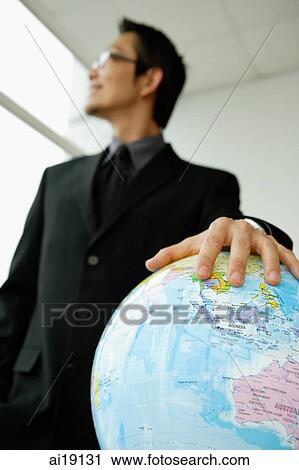 Stock Image - Businessman with hand on globe, looking away. Fotosearch