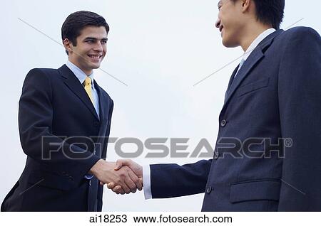 Stock Image - Businessmen shaking hands, low angle view. Fotosearch