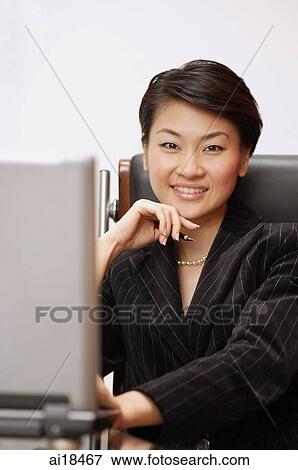 Businesswoman in office, sitting in front of laptop, looking at camera View Large Photo Image Stock Photo - Businesswoman in office, sitting in front of laptop, looking at camera. Fotosearch