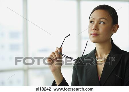 Stock Image - Businesswoman looking away, holding glasses. Fotosearch