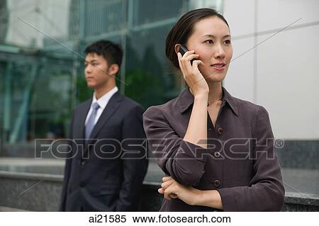 Businesswoman on mobile phone, man in the background View Large Photo Image Stock Photography - Businesswoman on mobile phone, man in the background. Fotosearch
