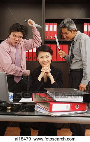 Businesswoman sitting at desk, smiling at camera, male executives behind her, holding knives View Large Photo Image Stock Photo - Businesswoman sitting at desk, smiling at camera, male executives behind her, holding knives. Fotosearch
