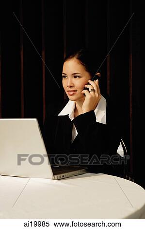 Businesswoman sitting in restaurant using mobile phone and laptop View Large Photo Image Stock Photography - Businesswoman sitting in restaurant using mobile phone and laptop. Fotosearch