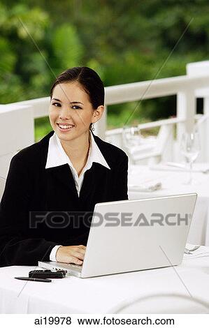 Stock Photo - Businesswoman sitting with laptop, looking at camera. Fotosearch