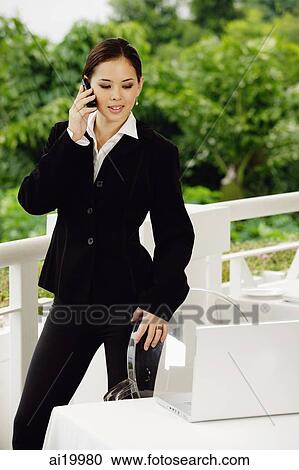 Businesswoman standing, using mobile phone, looking at laptop on table in front of her View Large Photo Image Stock Image - Businesswoman standing, using mobile phone, looking at laptop on table in front of her. Fotosearch