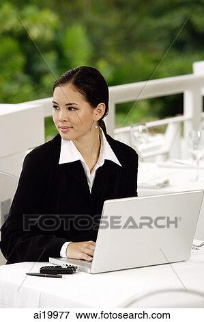 Stock Photo - Businesswoman with laptop, sitting in restaurant, looking away. Fotosearch