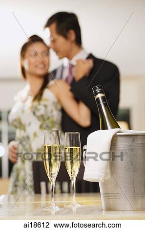 Champagne glasses and bottle in foreground, couple in background View Large Photo Image Stock Image - Champagne glasses and bottle in foreground, couple in background. Fotosearch