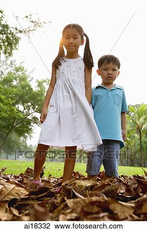 Stock Image - Children standing on pile of leaves, looking at camera. Fotosearch