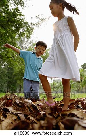 Stock Image - Children walking on pile of leaves in park. Fotosearch