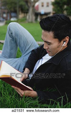Stock Image - College student lying on grass, reading a book. Fotosearch