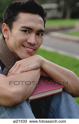 Stock Image - College student sitting on grass, looking at camera. Fotosearch