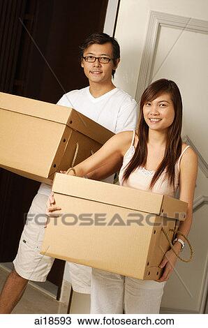 Stock Image - Couple at home, carrying boxes, smiling at camera. Fotosearch