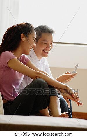 Couple at home, looking at mobile phone View Large Photo Image Stock Photography - Couple at home, looking at mobile phone. Fotosearch