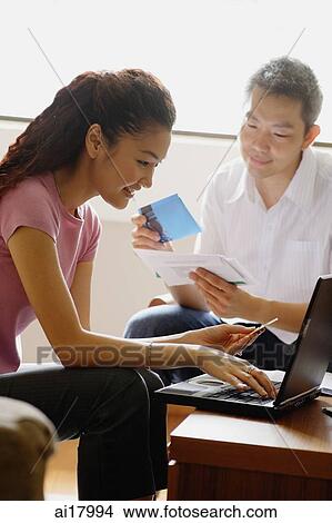 Picture - Couple at home, woman using laptop, man going through bills. Fotosearch