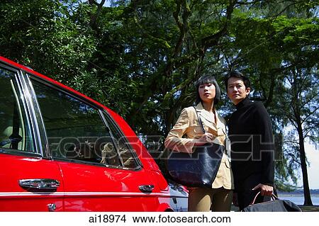 Picture - Couple carrying bags, standing next to red car. Fotosearch