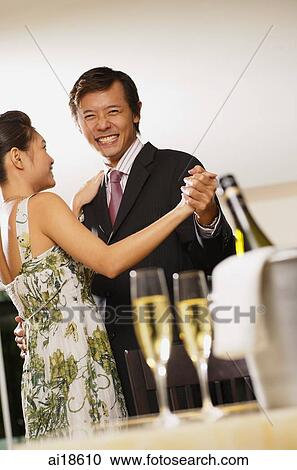 Stock Image - Couple dancing, champagne glasses and bottle in foreground. Fotosearch