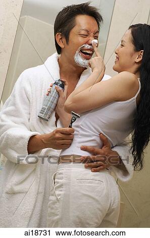 Stock Image - Couple embracing, woman applying shaving cream on man's nose. Fotosearch