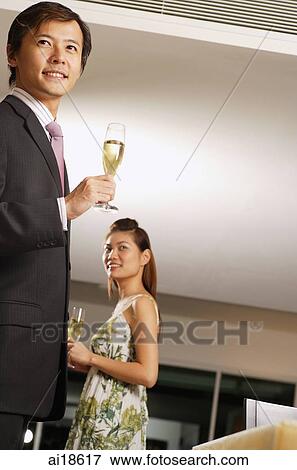 Couple holding champagne glasses, standing apart, low angle view View Large Photo Image Stock Photo - Couple holding champagne glasses, standing apart, low angle view. Fotosearch