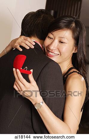 Picture - Couple hugging, woman looking at ring in box. Fotosearch