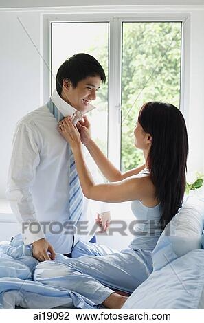 Stock Image - Couple in bedroom, woman adjusting man's tie. Fotosearch