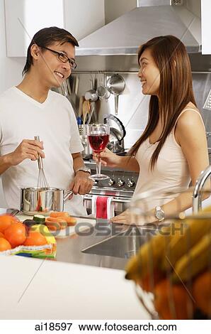 Couple in kitchen, man cooking, woman holding wine glass View Large Photo Image Stock Photo - Couple in kitchen, man cooking, woman holding wine glass. Fotosearch