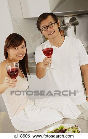 Couple in kitchen, raising wine glasses towards camera View Large Photo Image Stock Photography - Couple in kitchen, raising wine glasses towards camera. Fotosearch