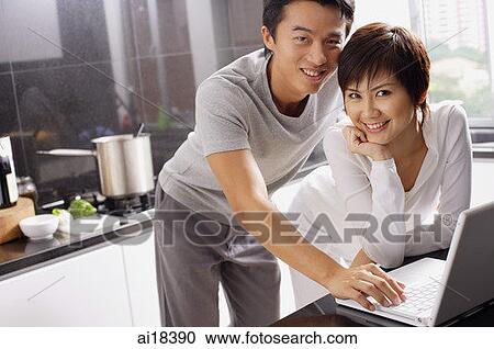Couple in kitchen, using laptop, smiling at camera View Large Photo Image Stock Image - Couple in kitchen, using laptop, smiling at camera. Fotosearch